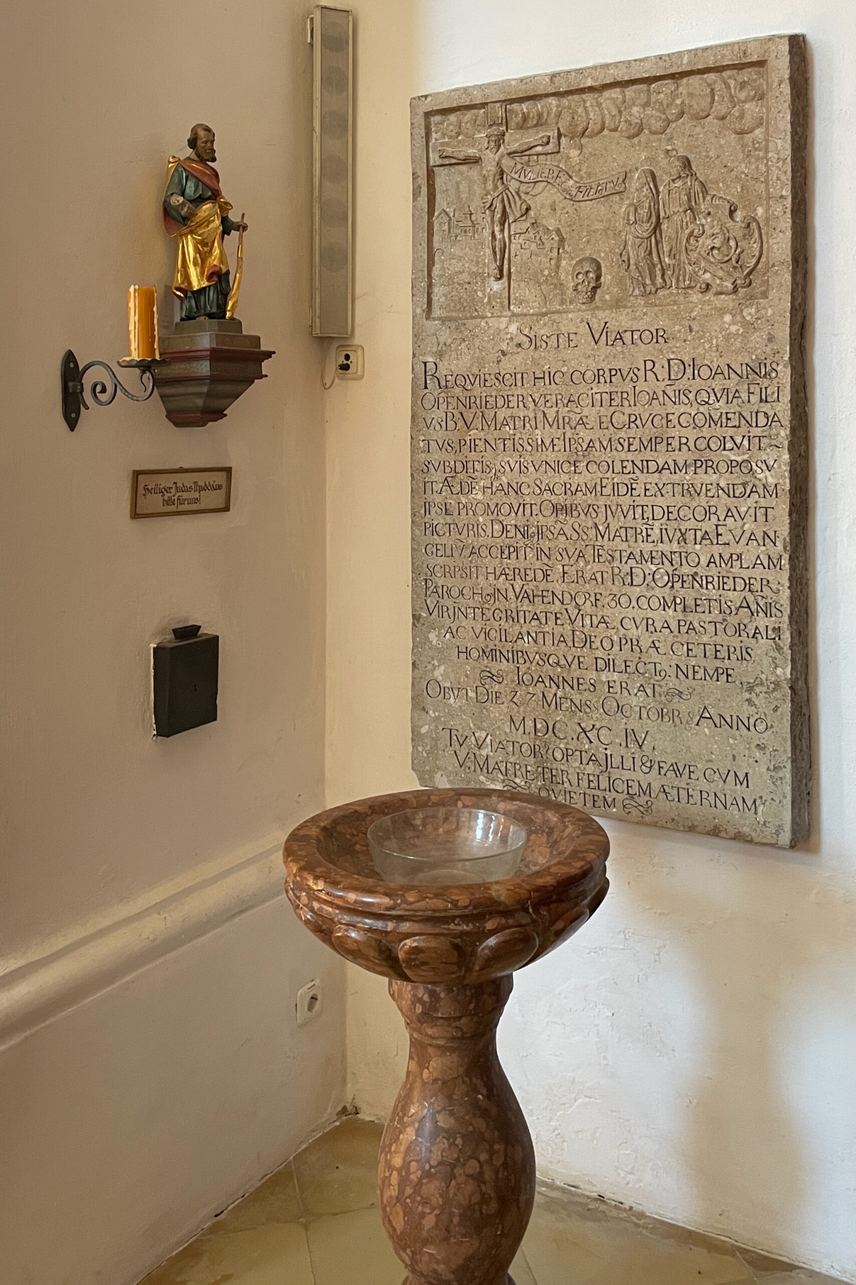 Das Epitaph des Pfarrers Johannes Oppenrieder an der Kirchenwand, mit dem Becken davor.