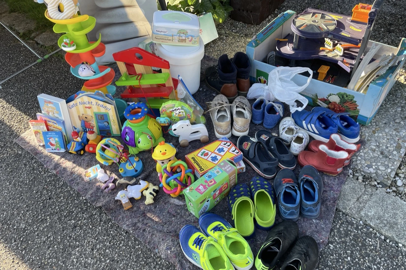 Spielzeug, Kinderbücher und Schuhe auf einer Decke beim Flohmarkt.