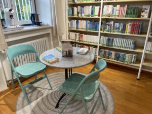 Zwei türkisfarbene Stühle und ein runder Tisch vor Bücherregalen in der Ratsch- und Leseecke.
