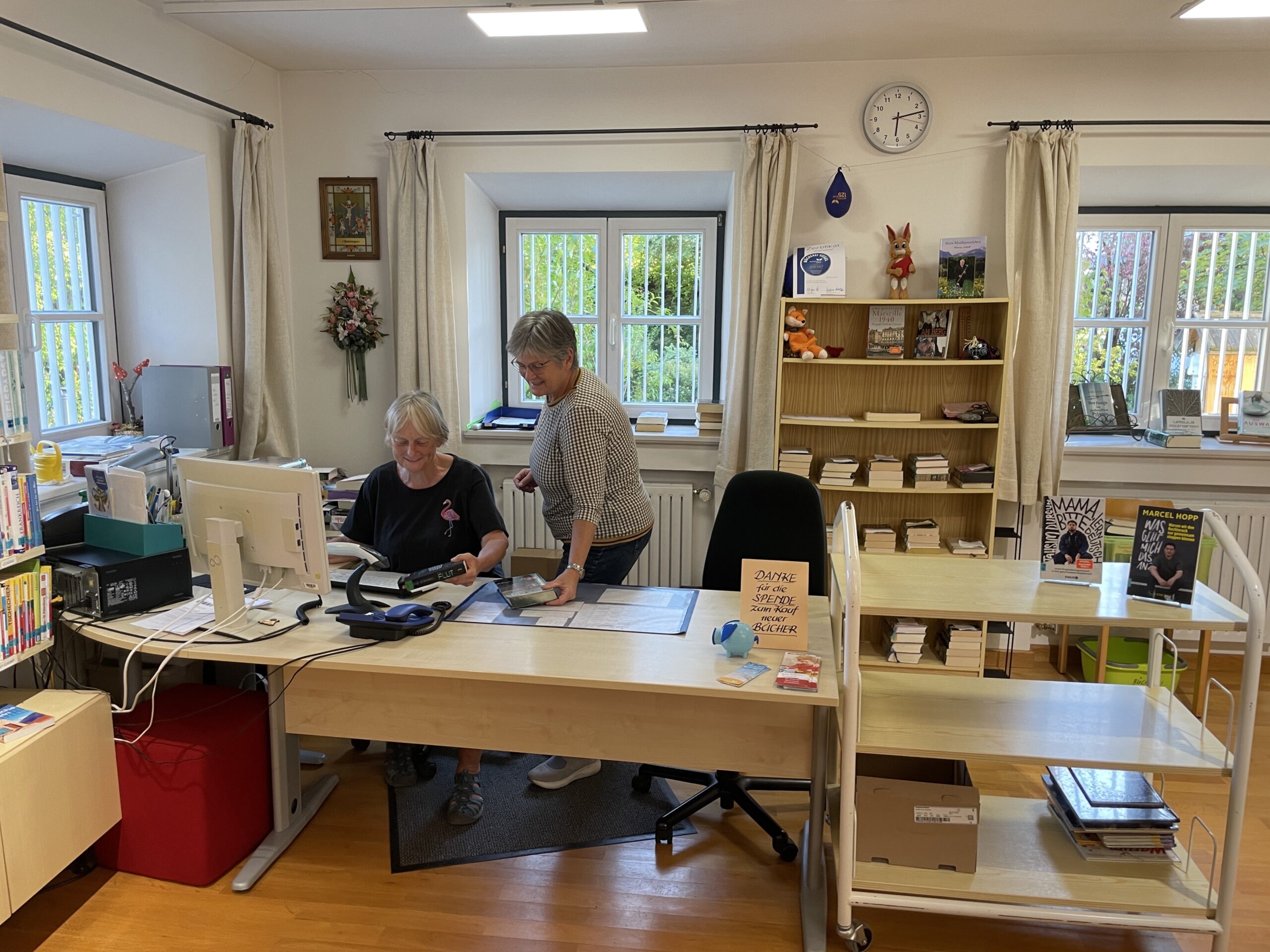 Christa Schmid und eine ehrenamtliche Mitarbeiterin arbeiten an der Ausleihtheke der Gemeindebücherei.