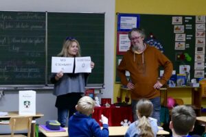 Zwei Erwachsene stellen in einer Schulklasse die Ergebnisse einer Mundarterhebung vor