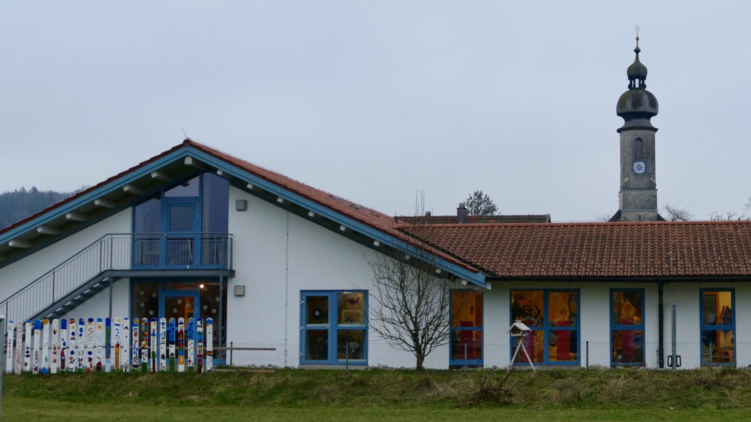 Gebäude des Kindergartens Maria Himmelfahrt in Vachendorf mit Kirchturm im Hintergrund