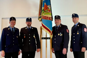 Vier Feuerwehrmänner vor der Vereinsfahne