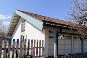 Helles Gebäude mit Satteldach, Garagentor und farbigem Zaun