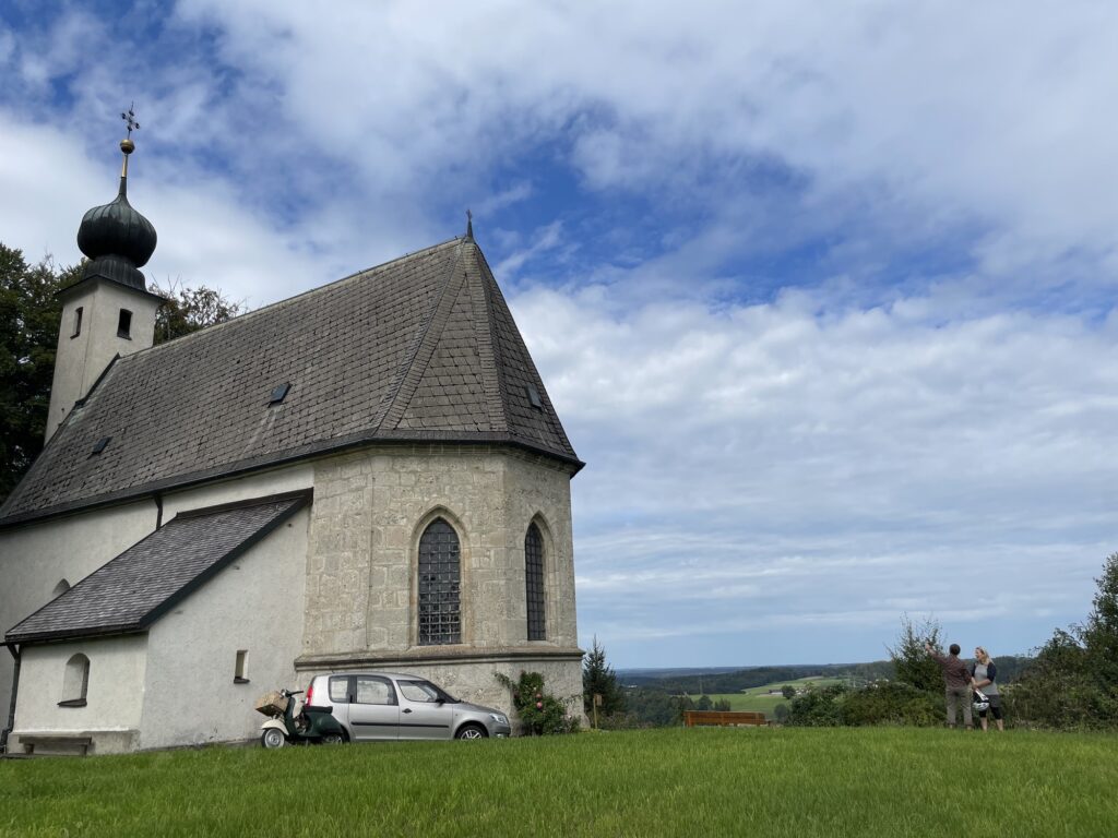Außenansicht der Kirche St. Georg am Berg mit Zwiebelturm und Blick über die Landschaft.