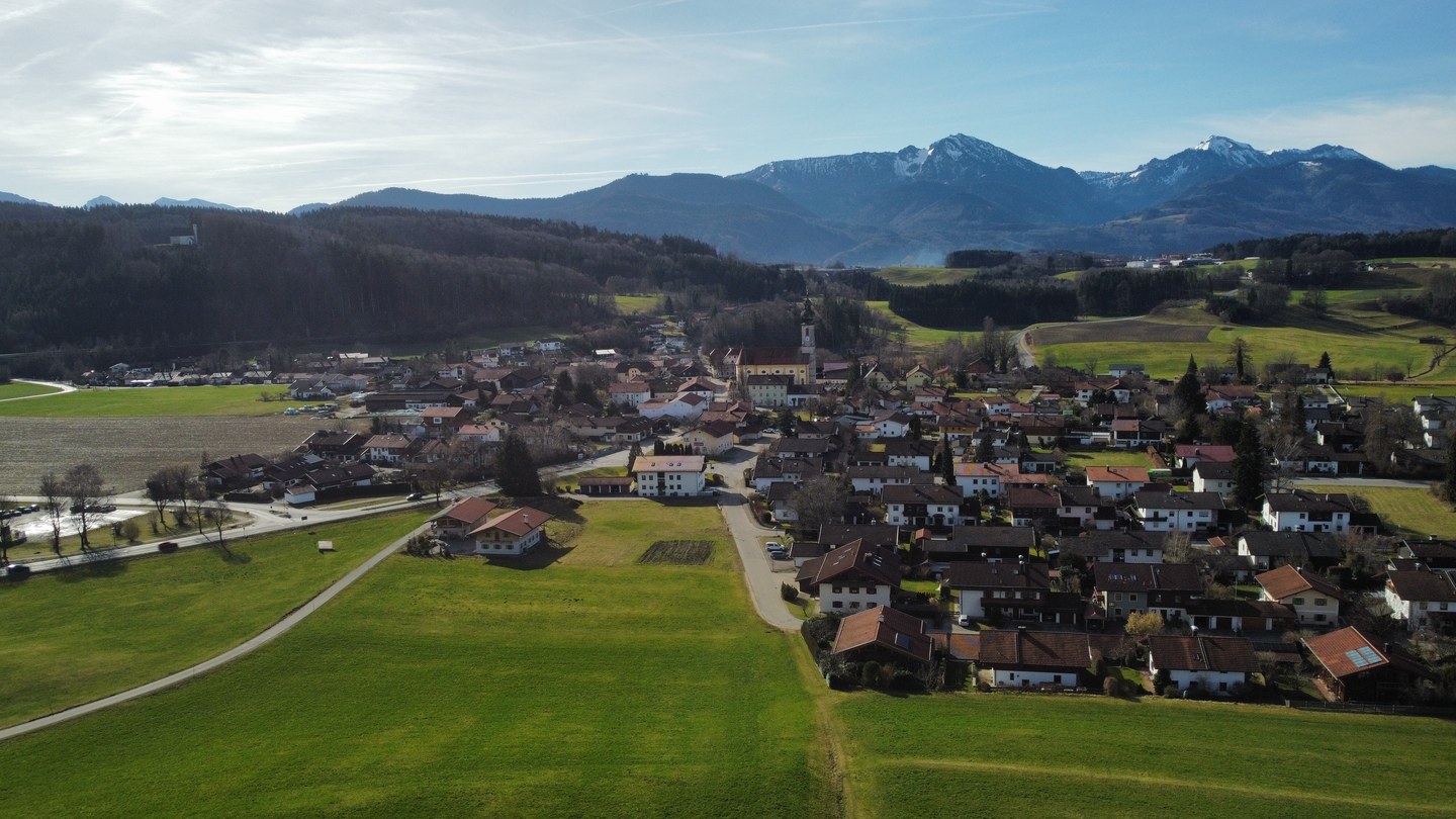 Luftbild von Vachendorf mit der Pfarrkirche im Ortskern und Bergen im Hintergrund.