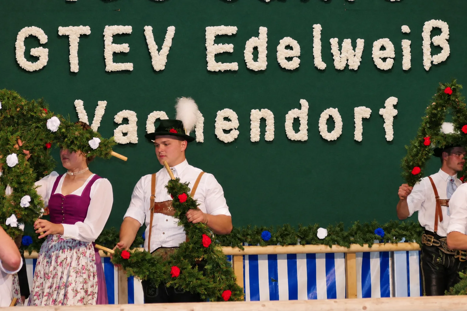 Mitglieder des GTEV Edelweiß Vachendorf in Tracht mit geschmückten Kränzen vor dem Vereinsnamen.