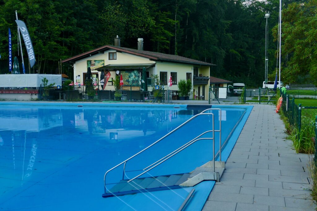 Das gefüllte Becken des Vachendorfer Freibads mit Einstiegstreppe und Betriebsgebäude.