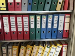 Beschriftete rote, grüne, blaue und gelbe Ordner der Heimatkundlichen Stoffsammlung Franz Liebl im Regal.