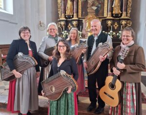 Sechs Mitwirkende des Vachendorfer Zither-Ensembles mit ihren Instrumenten vor dem Altar der Pfarrkirche Vachendorf.