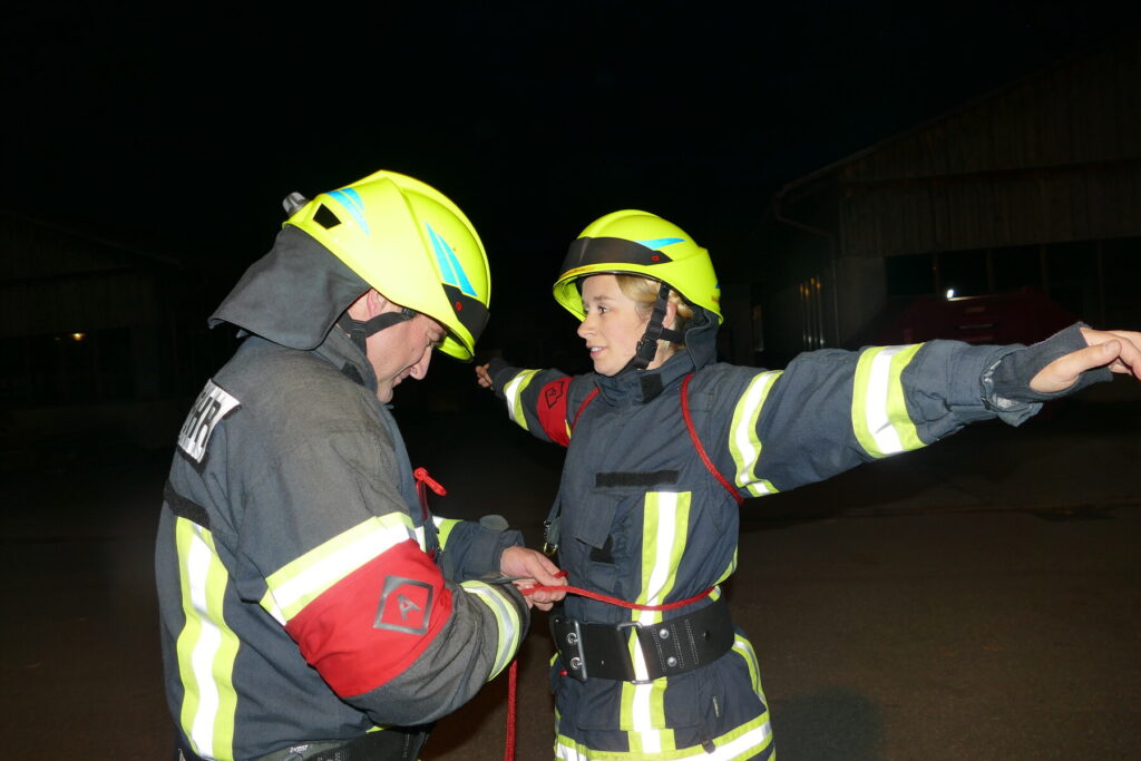 Zwei Feuerwehrmitglieder zeigen das Anlegen einer Feuerwehrleine am Körper.