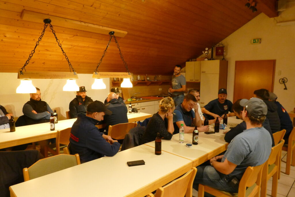 Teilnehmer und Prüfer sitzen nach der Leistungsprüfung gemeinsam im Feuerwehrhaus.