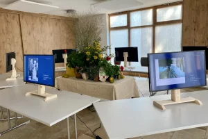 Sechs Bildschirme auf weißen Tischen um einen Blumenschmuck.