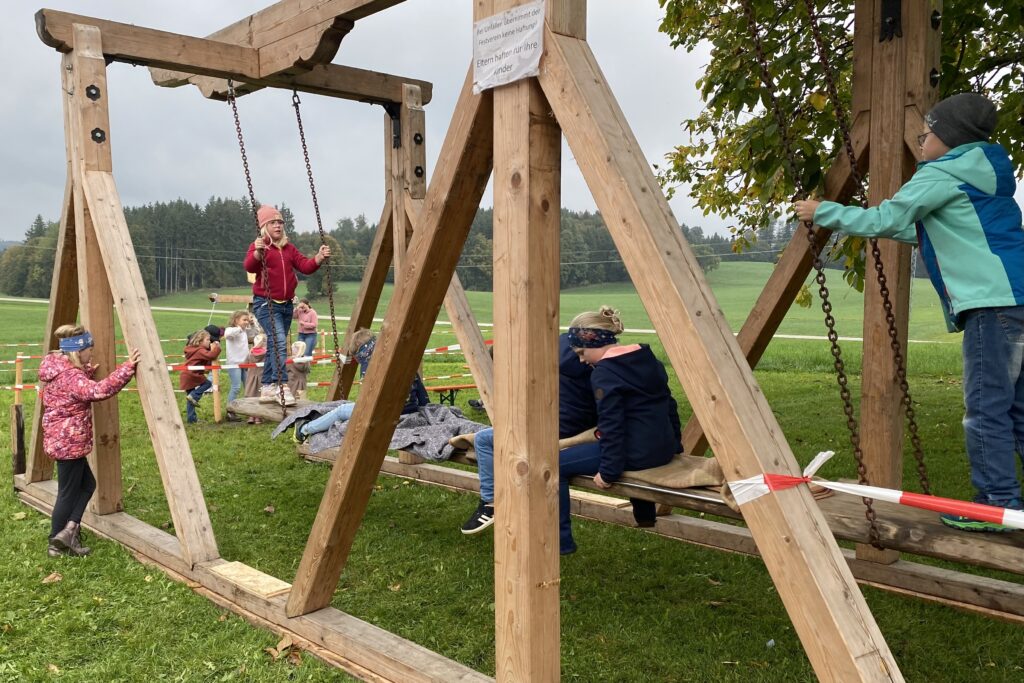 Kinder auf einer großen hölzernen Kirtahutschen auf der Wiese.