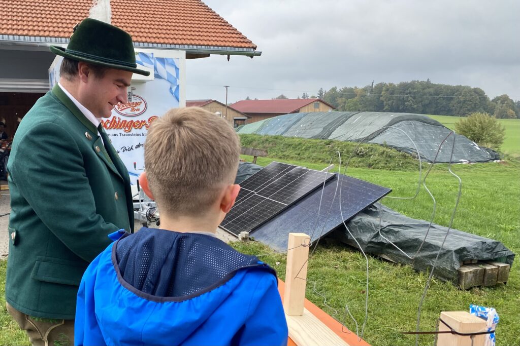 Ein Kind am Geschicklichkeitsspiel heißer Draht neben einem Mann in Tracht.