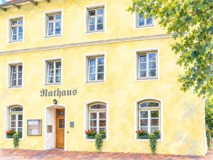 Aquarellansicht der Rathausfassade in Vachendorf mit Schriftzug Rathaus, Eingang und Blumenkästen.