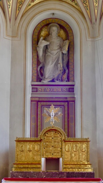 Im Zentrum des Altarraums thront die Statue des Kirchenpatrons St. Aegidius mit der Hirschkuh – ein klassisches Attribut seiner Legende – über einem reich vergoldeten Tabernakel, der von der Taube des Heiligen Geistes bekrönt wird. Bergen st aegidius altar