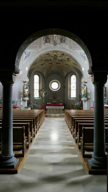 Der Blick durch den Arkadenbogen auf den Altarraum von St. Maximilian enthüllt ein fein austariertes Zusammenspiel aus romanisierender Architektur, reicher Gewölbemalerei und ruhiger Raumkomposition. Grabenstaett st maximilian gesamteindruck