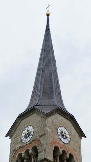 Der Turm wird von einem steilen, elegant geschwungenen Spitzhelm bekrönt, dessen Schieferdeckung in feinen Bahnen aufsteigt und in einem vergoldeten Kreuz gipfelt. Grabenstaett st maximilian turm