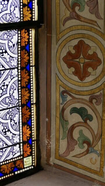 Im Detail zeigt sich das harmonische Zusammenspiel von ornamentaler Wandmalerei und leuchtendem Glasdekor: florale Formen, feine Linien und warme Farbtöne verschmelzen zu einem Gesamtkunstwerk aus Licht und Farbe. Grabenstaett st maximilian wandbild
