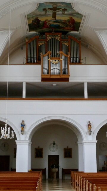 Die Orgel in der Kirche Mariä Himmelfahrt in Vachendorf schwebt über dem Eingang, eingerahmt von einem Passionsfresko und dem goldenen Schriftzug „Maria gratia plena“. Blick nach hinten